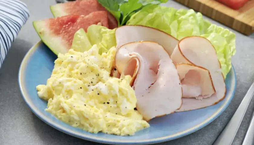 En blå tallrik med äggröra, kalkonpålägg, sallad och vattenmelon. En hälsosam 5:2 frukost för en bra start på dagen.