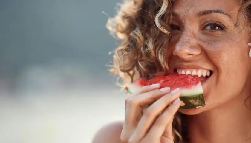 En kvinna med lockigt hår njuter av en saftig bit vattenmelon, ett bevis på att vattenmelon nyttigt är sant.