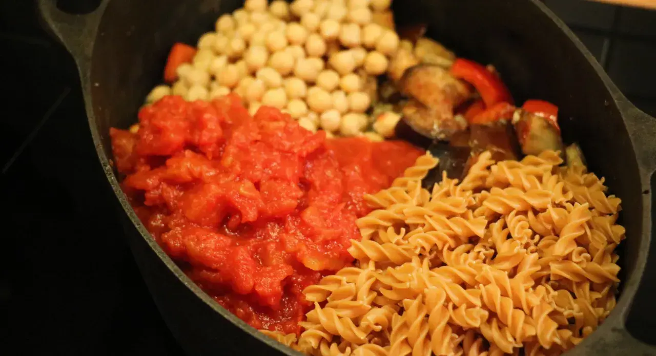 En proteinrik matlåda recept med pasta, kikärtor, tomatsås och grönsaker i en gjutjärnspanna.