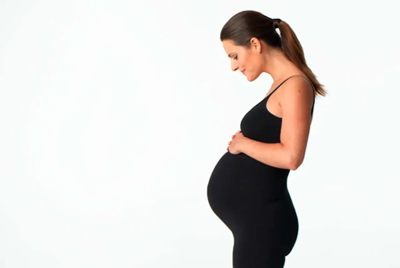 Gravid kvinna i svart klänning håller om sin mage. Hon ser kärleksfullt ner på sin honung.