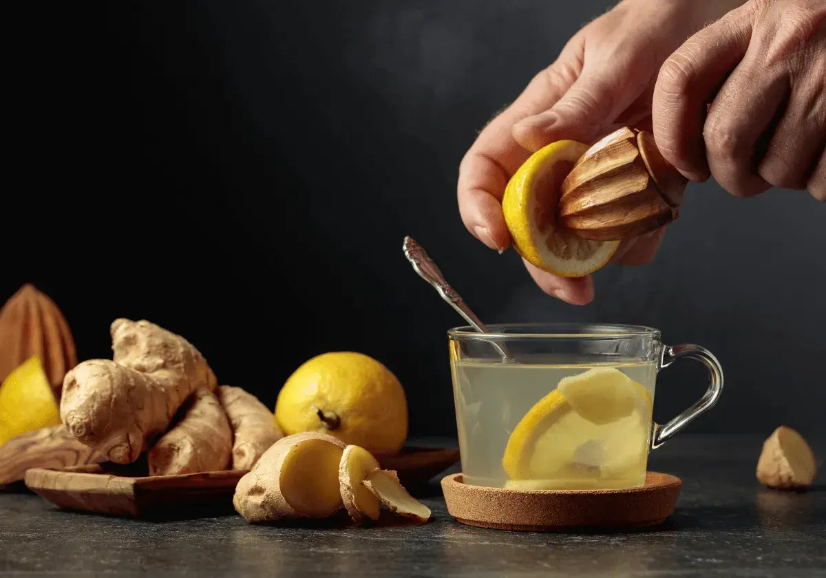 En hand pressar citron i en kopp med varmt citronvatten på morgonen. Ingefära och citroner ligger bredvid.