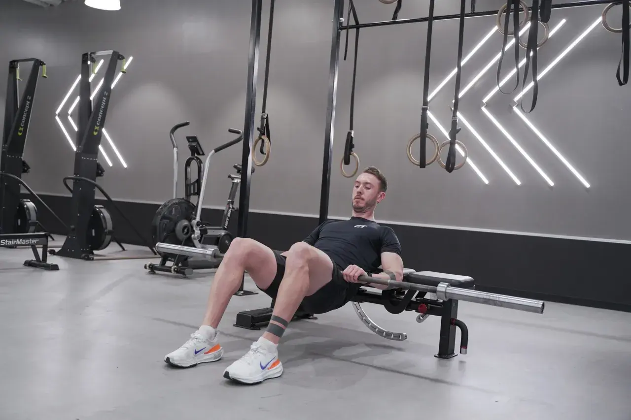Man utför höftlyft med skivstång för att bygga muskler i rumpan. Träningspasset sker i ett modernt gym.