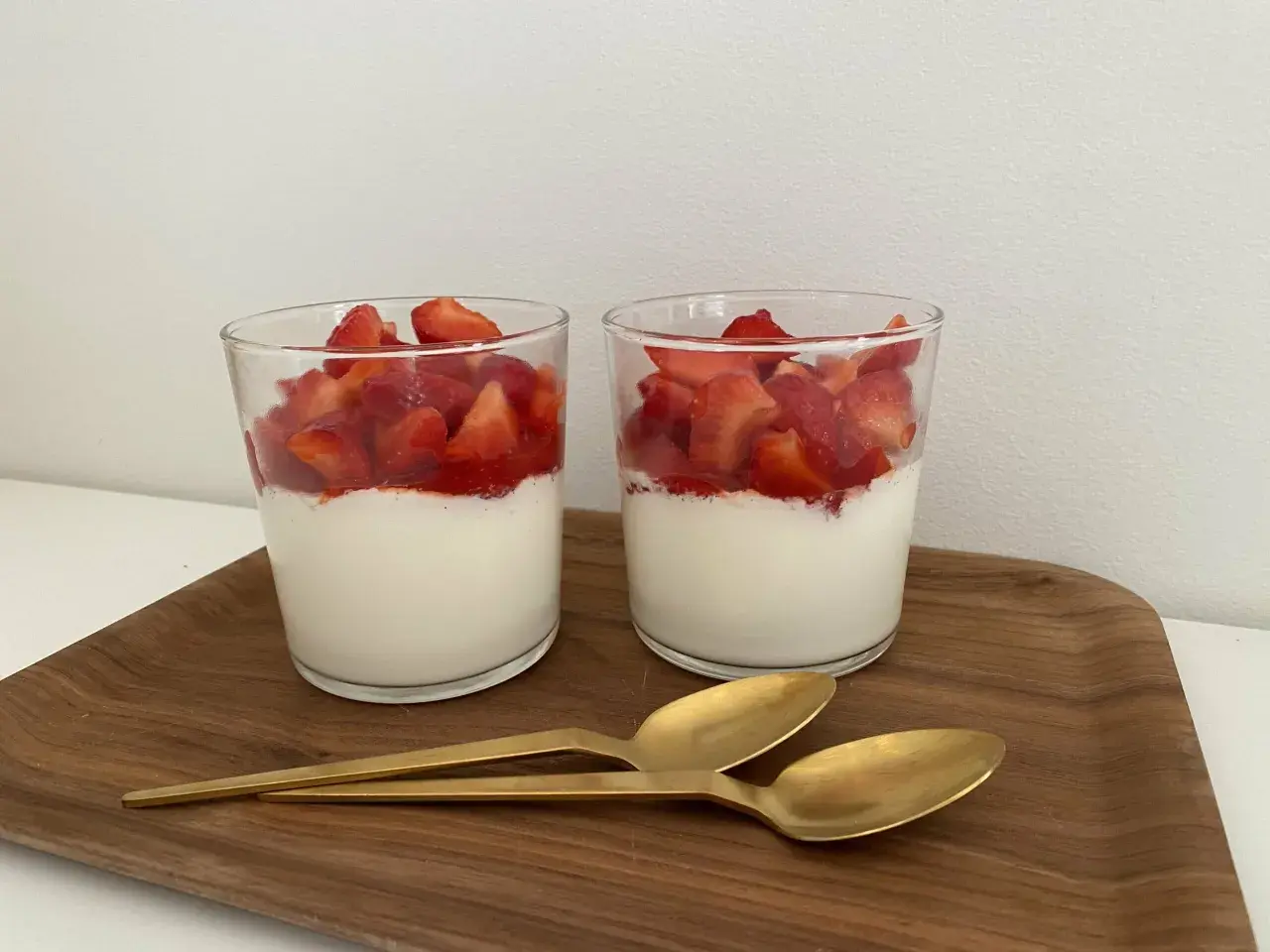 Två glas med grädde och färska jordgubbar, en läcker dessert som passar även för diabetiker typ 2. Två guldfärgade skedar ligger på en träbricka.