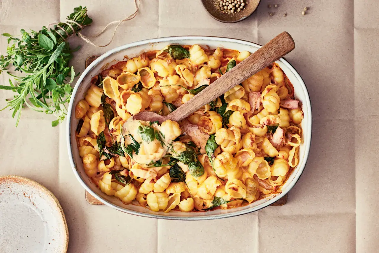 En krämig pastarätt med lax och spenat, perfekt för nyttiga recept. En träsked lyfter upp en portion ur ugnsformen.
