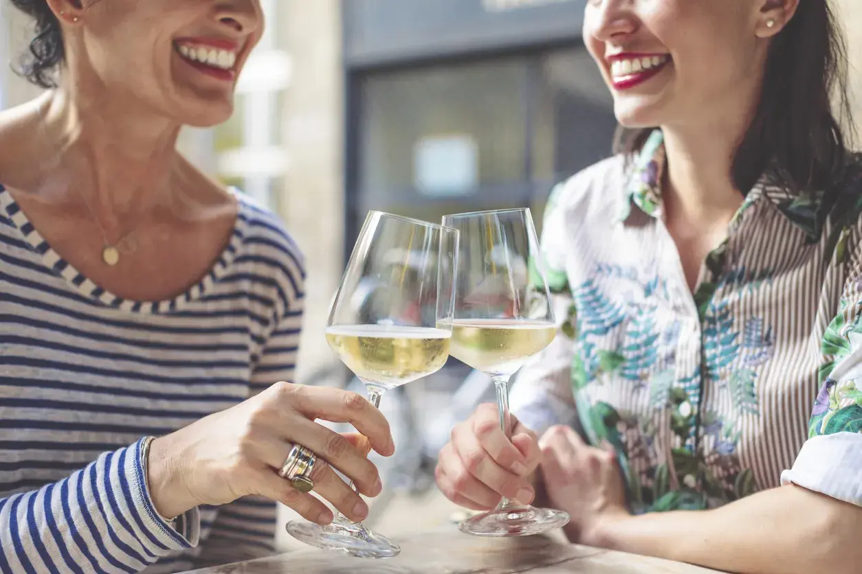 Två glada kvinnor skålar med vitt vin. En titt på kalorier alkohol tabell kan vara bra att ha i åtanke.