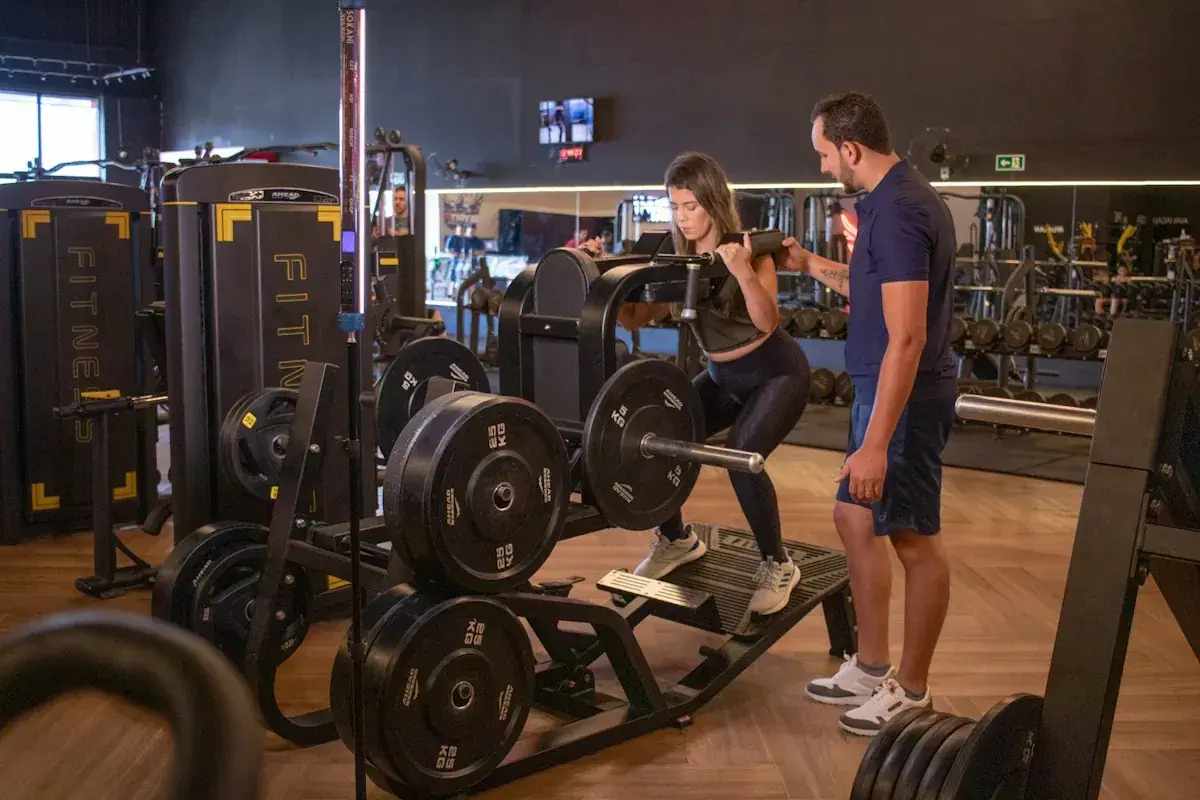 Kvinna utför benpress med instruktör vid sin sida, en del av ett push pull program.
