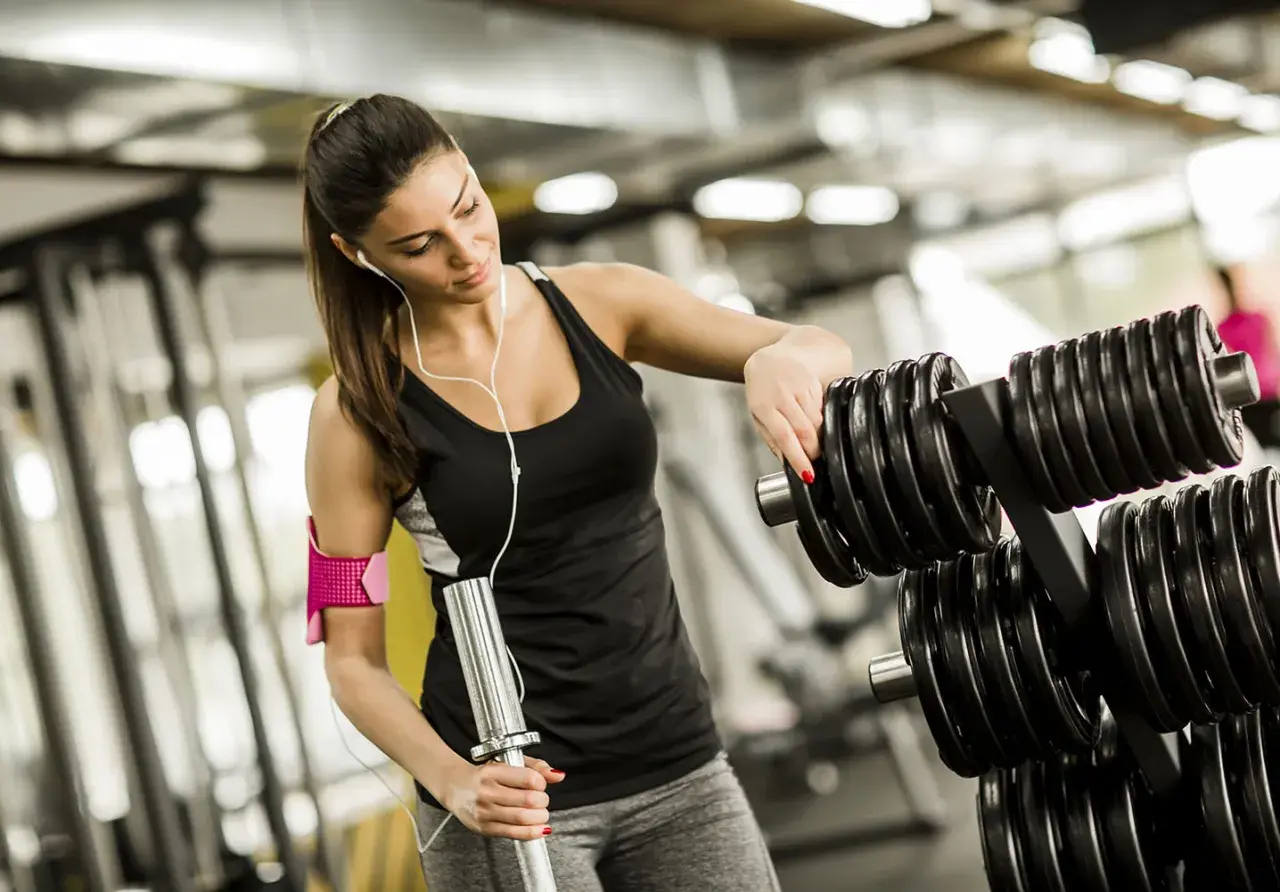 En kvinna väljer vikter på gymmet för sina reps och set.