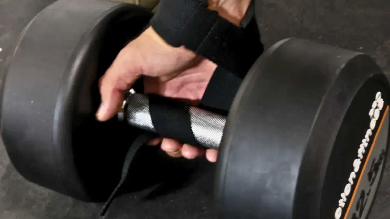 En hand med dragremmar gym greppar ett tungt hantelhandtag för ett stadigt lyft.