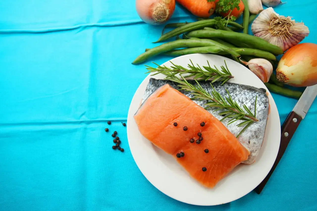 Laxfilé med rosmarin och pepparkorn, omgiven av grönsaker som morötter, haricots verts och vitlök. Perfekt d-vitamin mat för en hälsosam måltid.