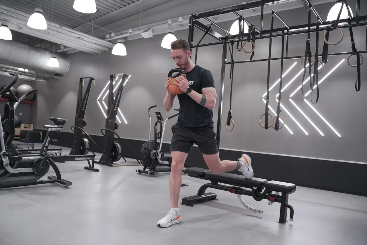 Man gör en utfall med kettlebell i ett modernt gym, perfekt för rumplyft.
