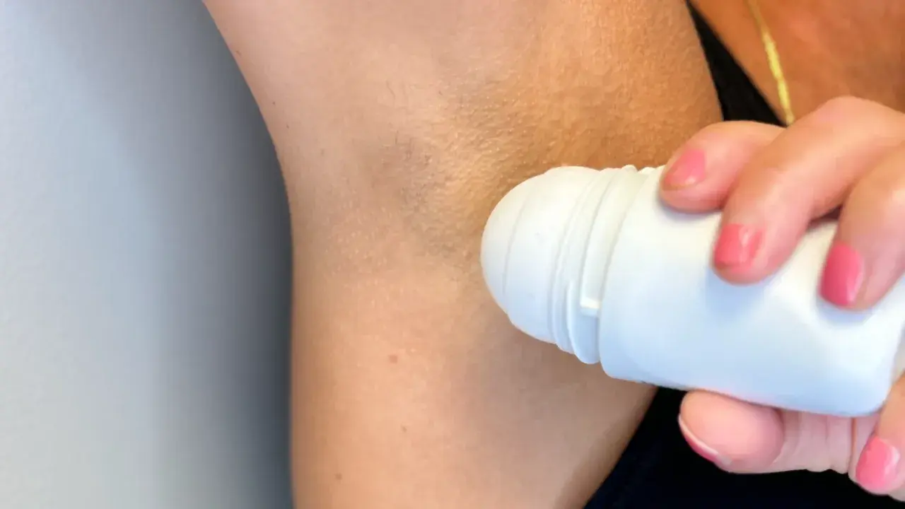 En person applicerar roll-on deodorant under armen. Trots deodoranten kan det ibland lukta svett.