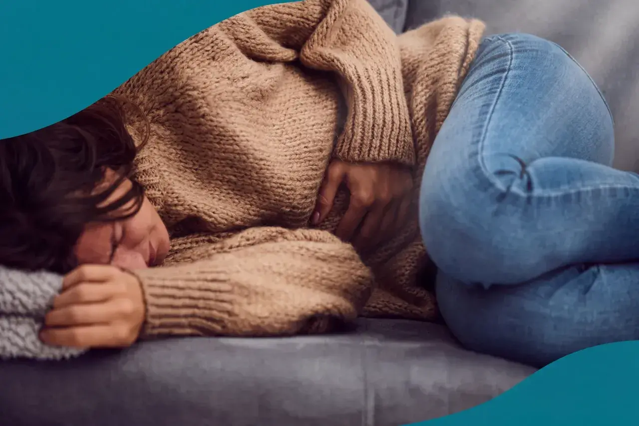 En kvinna med mörkt hår ligger hopkrupen på en soffa, med handen på magen. Hon ser ut att ha ont, vilket kan vara ett av många endometrios symtom.