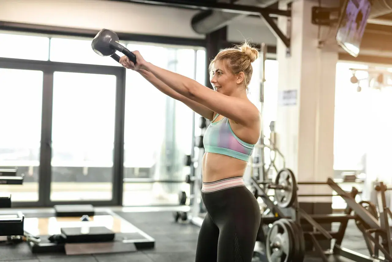 Kvinna utför kettlebell-svängar i gymmet. Bra gymtips för en helkroppsträning.
