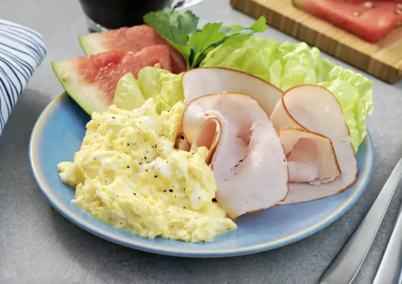 En blå tallrik med äggröra, kalkonpålägg, sallad och vattenmelon. En hälsosam 5:2 frukost för en bra start på dagen.