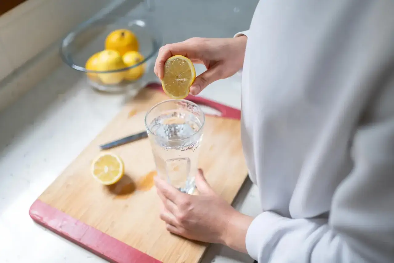 En hand pressar en citronhalva över ett glas vatten. En hälsosam start på dagen med citronvatten.
