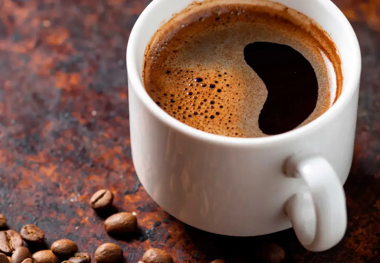 En vit kopp med varm en kopp kaffe koffein, omgiven av rostade kaffebönor på en rustik yta.