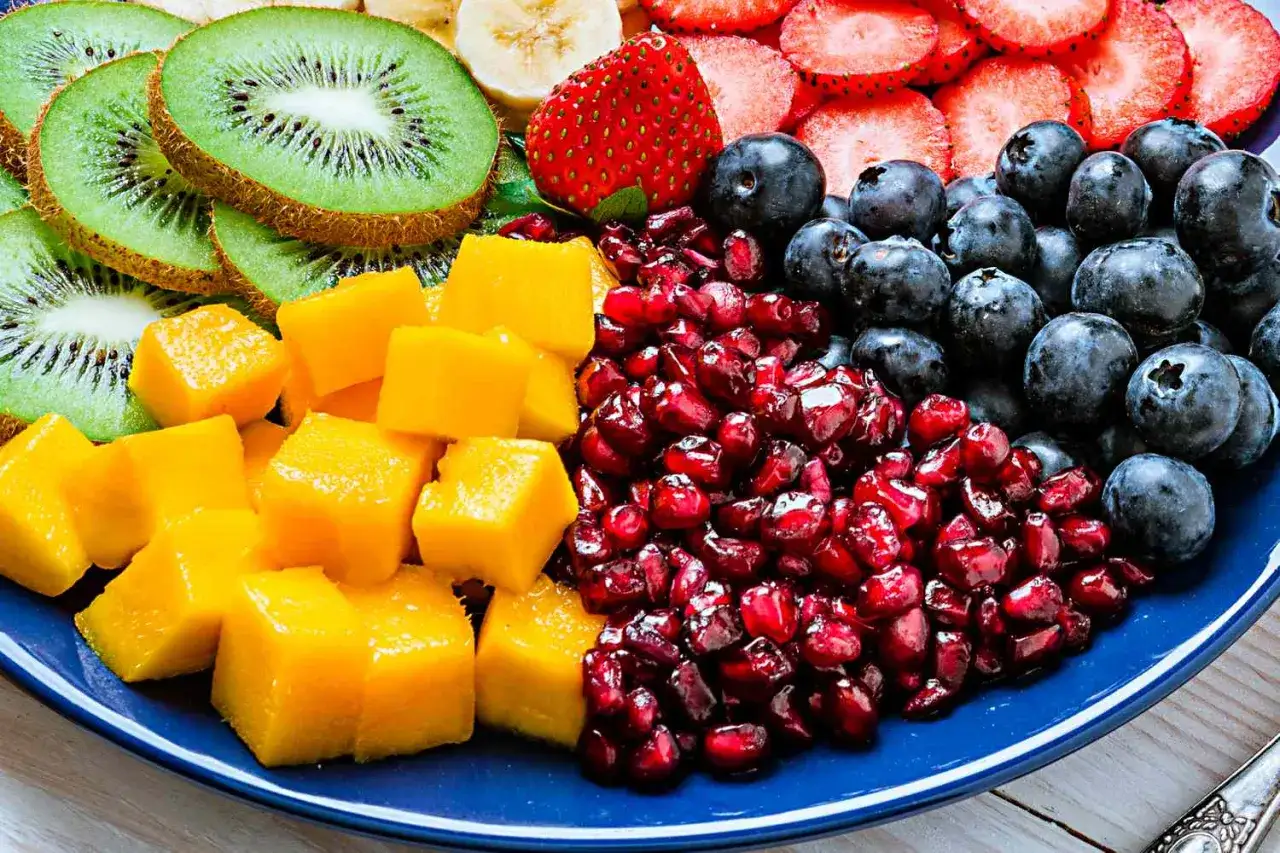 En blå tallrik fylld med kiwi, mango, granatäpple, blåbär, jordgubbar och banan. En färgsprakande och nyttigaste frukten för en energifylld start!