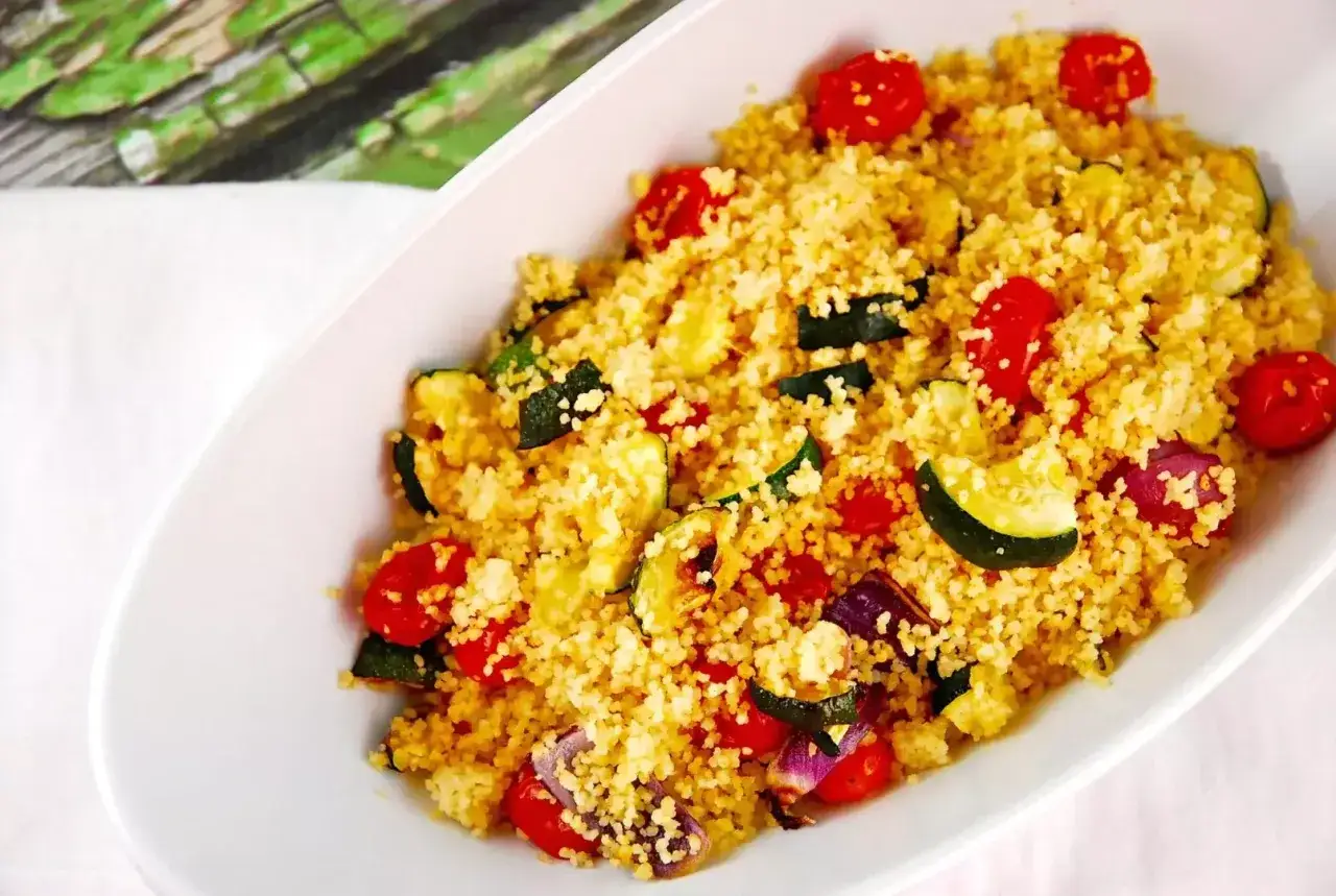 En skål med couscous nyttigt, blandad med körsbärstomater, zucchini och rödlök. En färgstark och hälsosam måltid.