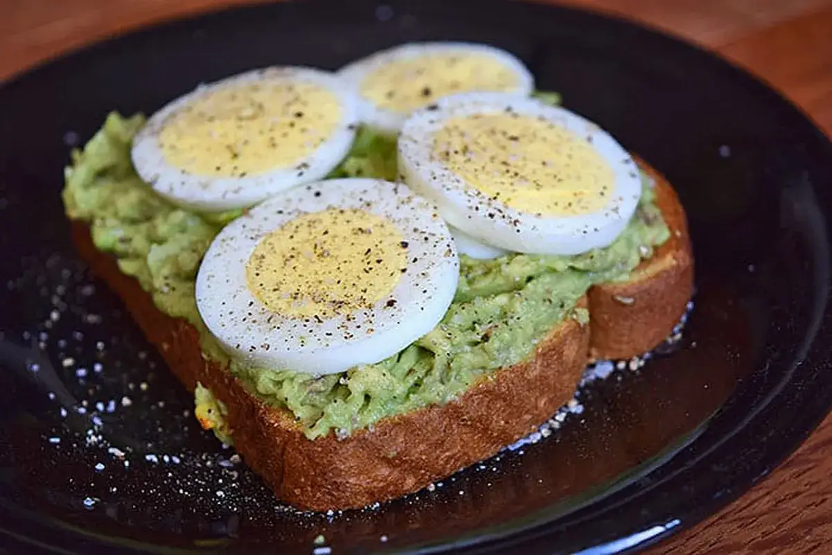 Rostat bröd med mosad avokado och äggskivor, strött med peppar. En hälsosam frukost som ger bra energi, trots avokado kalorier.
