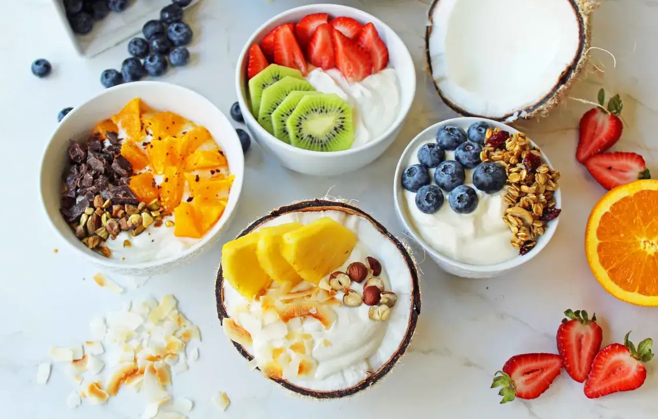 Frukostskålar med grekisk yoghurt nyttigt och färsk frukt som jordgubbar, kiwi, apelsin och ananas. Kokosflingor och nötter för extra crunch.