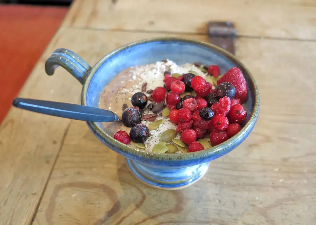 En blå skål med en smoothiebowl fylld med bär, kokosflingor och pumpakärnor. Bigarråer nyttigt och gott!