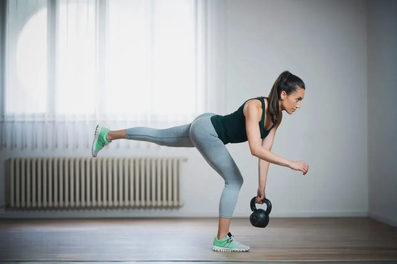 Kvinna tränar med kettlebell, fokuserar på baksida lår.