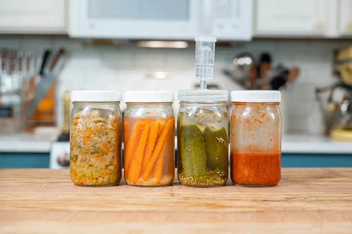 Fyra burkar med fermenterad mat: surk&aring;l, mor&ouml;tter, gurka och kimchi. En j&auml;sningsventil sitter p&aring; gurkburken.