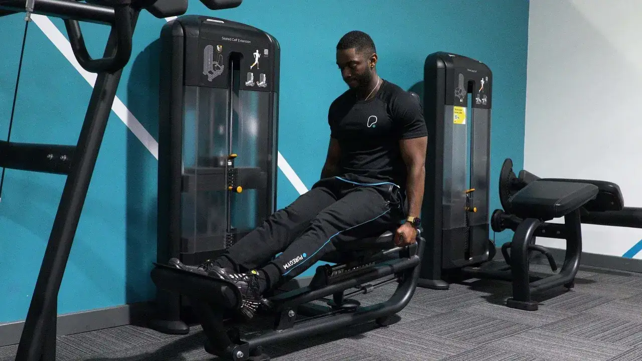 Man tränar sina små vader på en sittande vadpress i ett modernt gym.