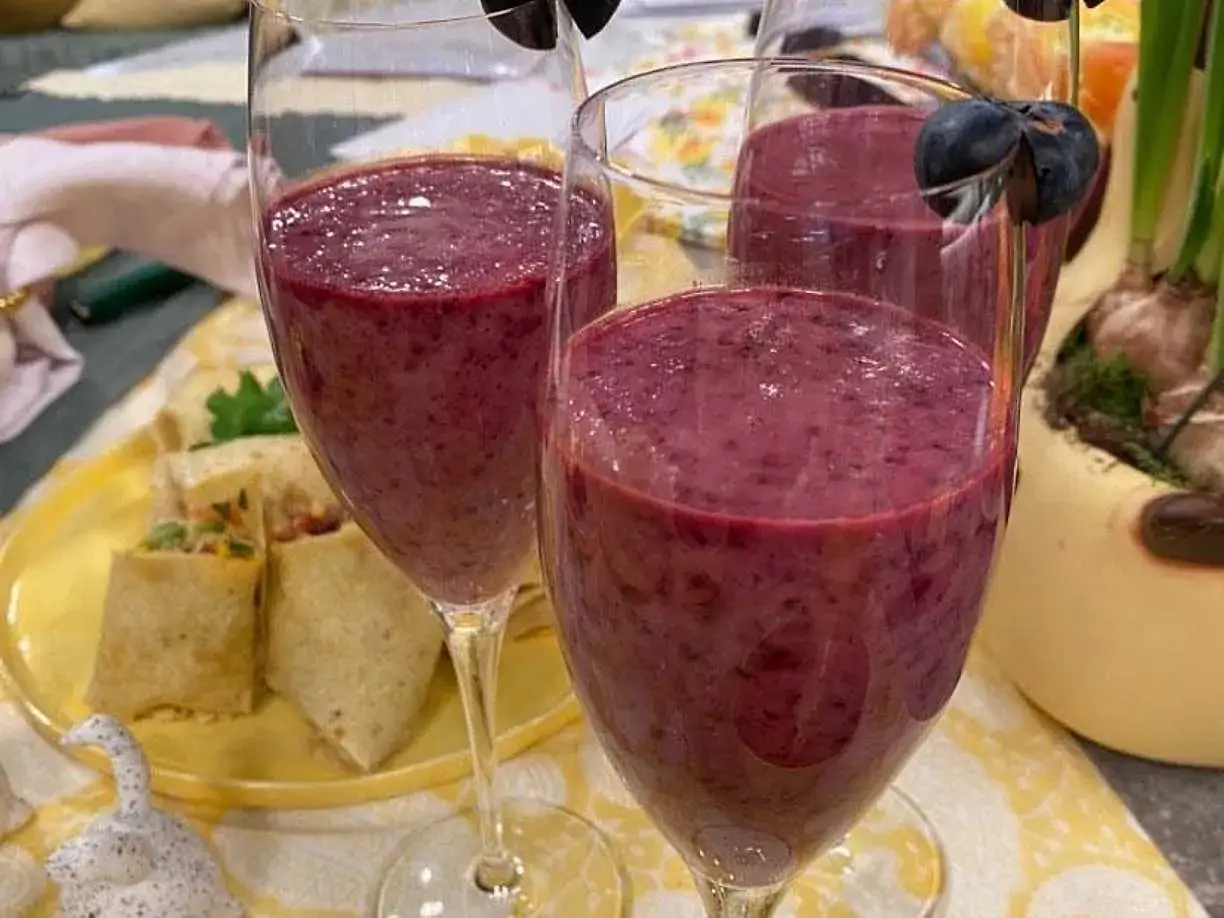 Två glas med en nyttig smoothie, dekorerad med blåbär. I bakgrunden syns små wraps på en gul tallrik.