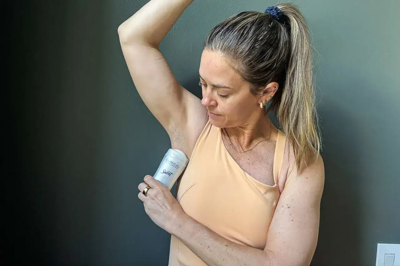 Kvinna applicerar deodorant under armen, hoppas att det inte luktar svett trots deo.