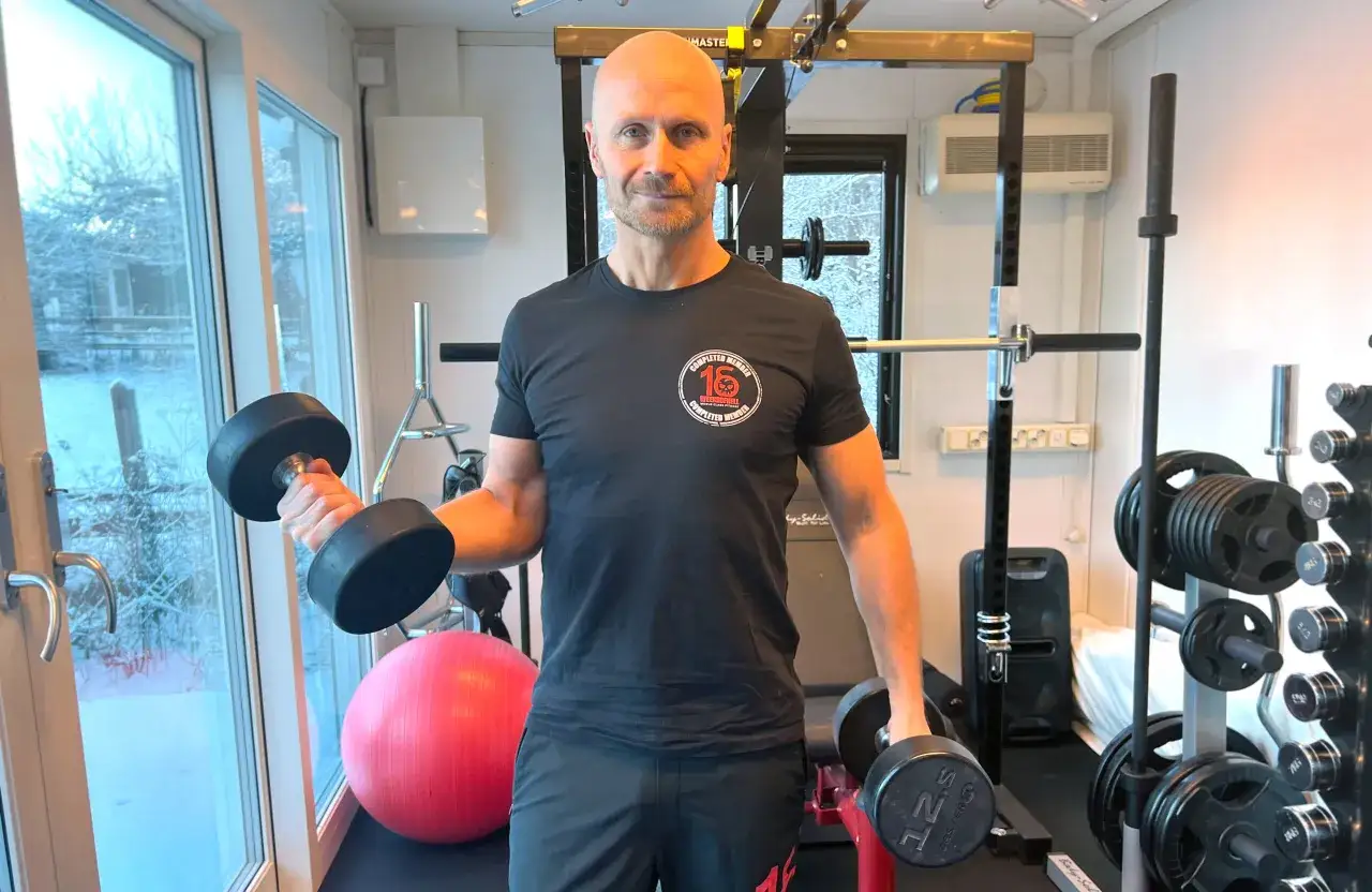 Man i hemmagym med hantlar, redo för 16 weeks of hell.