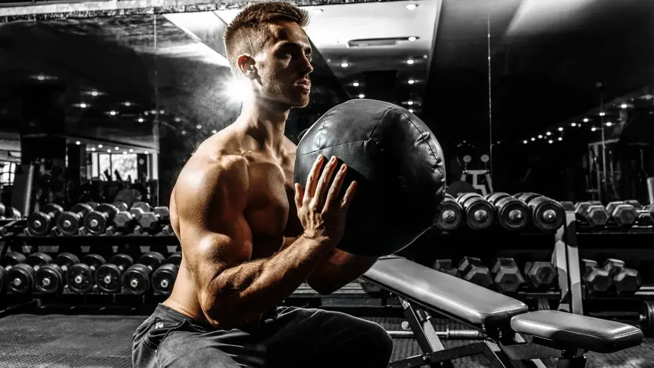 Muskulös man i gym håller en medicinboll. Träning kan motverka testosteron brist och ge energi.