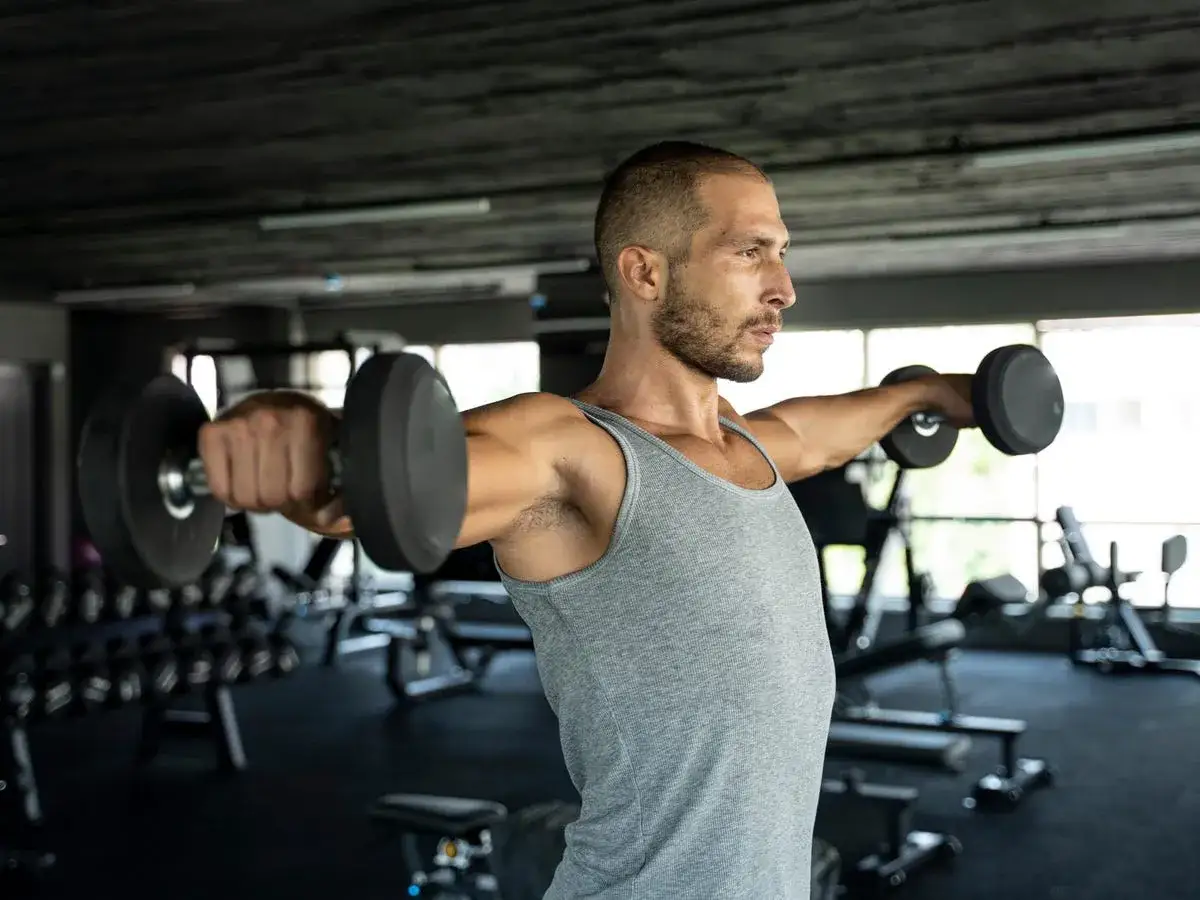 Man utf&ouml;r sidolyft med hantlar i gymmet. Bra gymtips f&ouml;r axeltr&auml;ning.