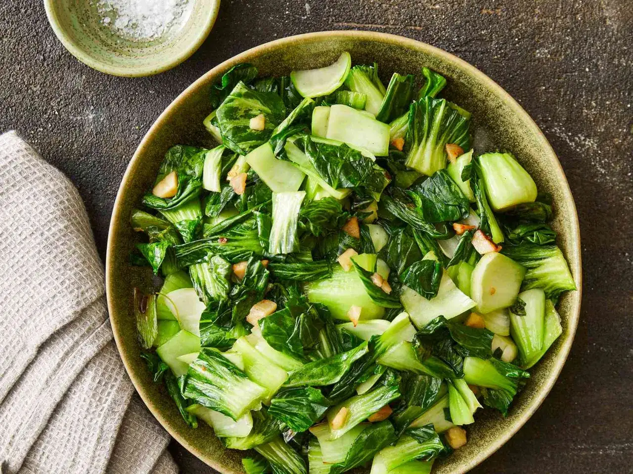 En skål med ångad pak choi, en nyttig och god grönsak, med vitlök och en nypa salt vid sidan.